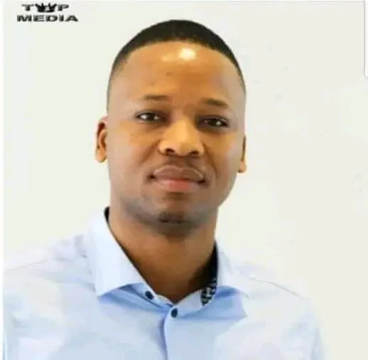 Homme souriant portant une chemise bleue clair sur fond blanc avec un logo en haut à gauche