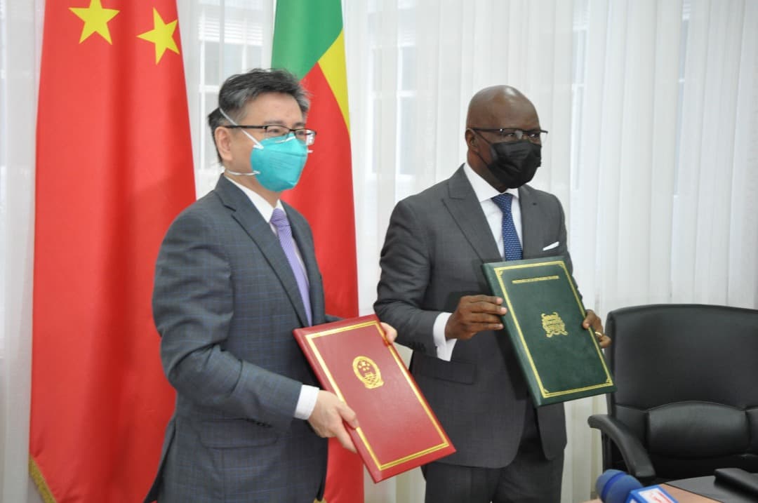 Deux hommes en costume et masque tenant des dossiers devant les drapeaux de la Chine et d’un autre pays