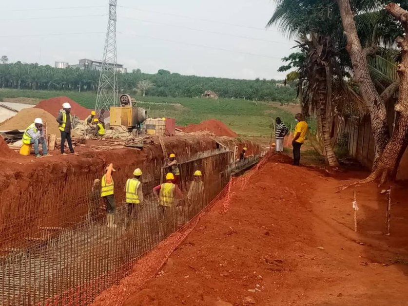 Ouvriers en tenue de chantier travaillent à la construction d une structure en béton sur un terrain rouge avec des arbres à droite
