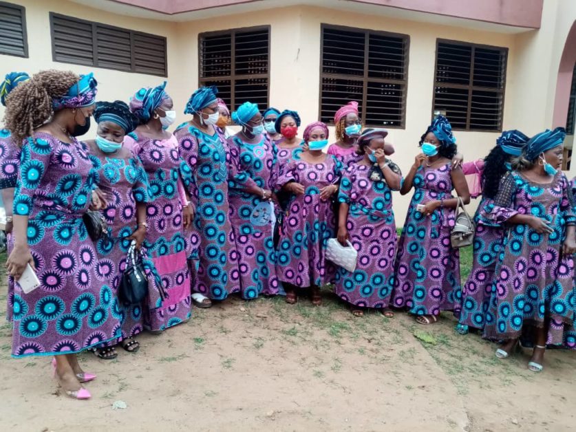 Groupe de femmes en robes et foulards assortis aux motifs colorés posant ensemble devant un bâtiment avec fenêtres entrouvertes