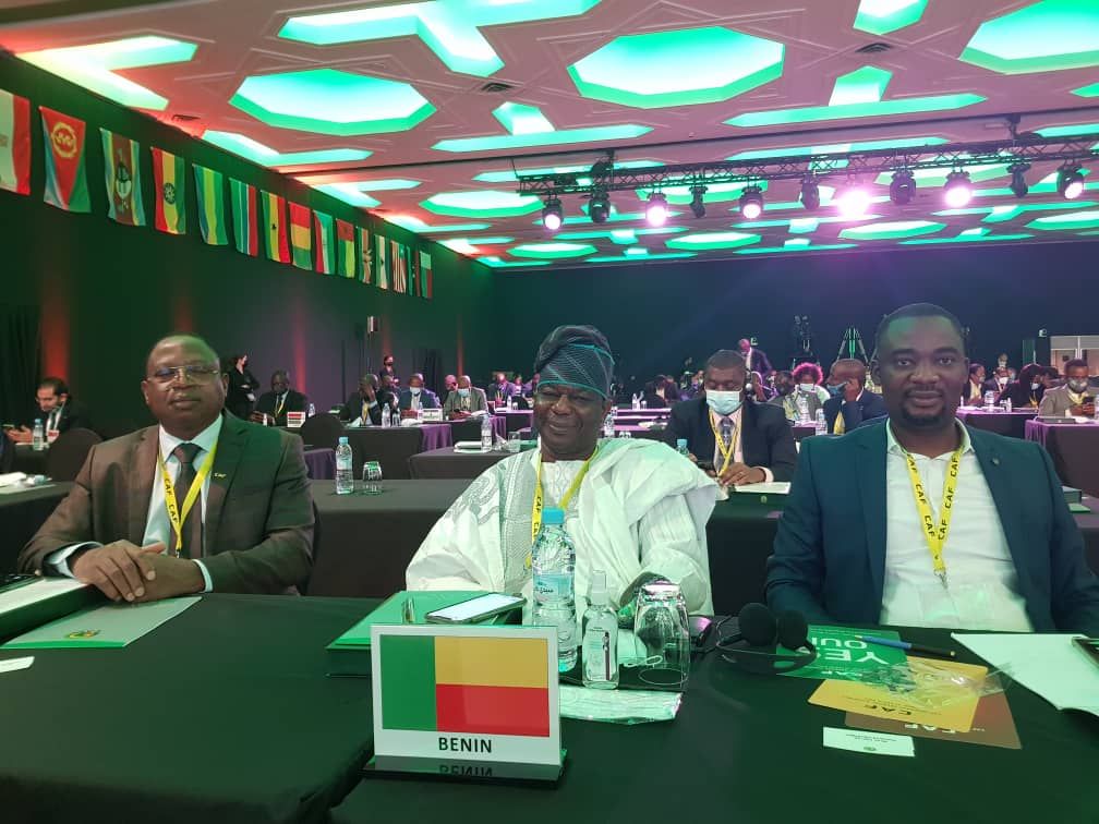 Trois délégués assis à une table avec un panneau portant le drapeau et le nom du Bénin lors d'une conférence internationale
