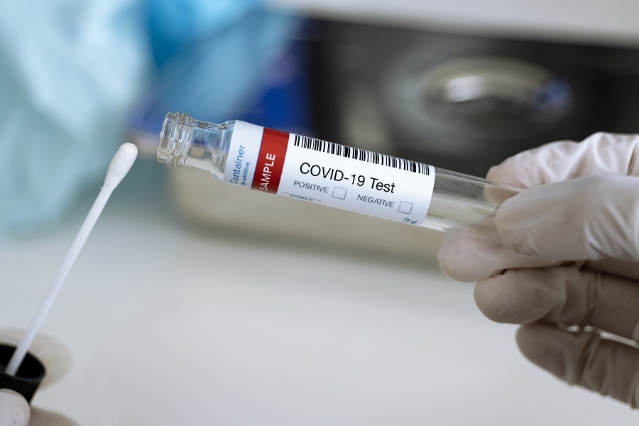 Main gantée tenant un tube de prélèvement marqué COVID-19 Test avec un écouvillon à proximité