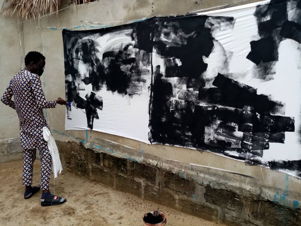 Un homme peint en noir sur une grande toile blanche accrochée à un mur extérieur en ciment
