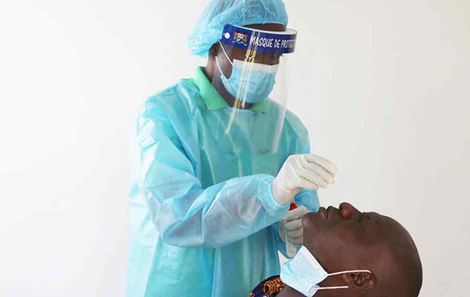 Un professionnel en tenue de protection prélève un échantillon nasal sur un patient assis pour un test médical