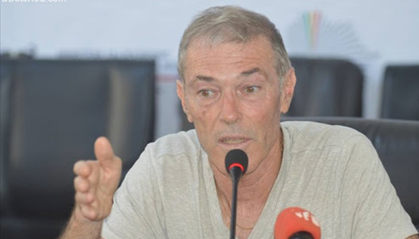 Homme aux cheveux courts grisonnants parlant devant un micro lors d une conférence de presse en intérieur