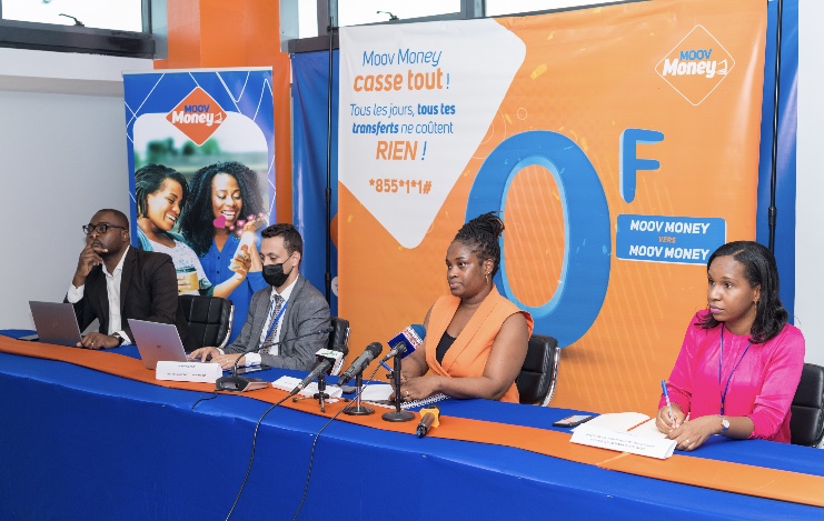 Quatre personnes, dont deux femmes et deux hommes, assises à une table avec micros et ordinateurs devant une banderole promotionnelle orange et bleue.