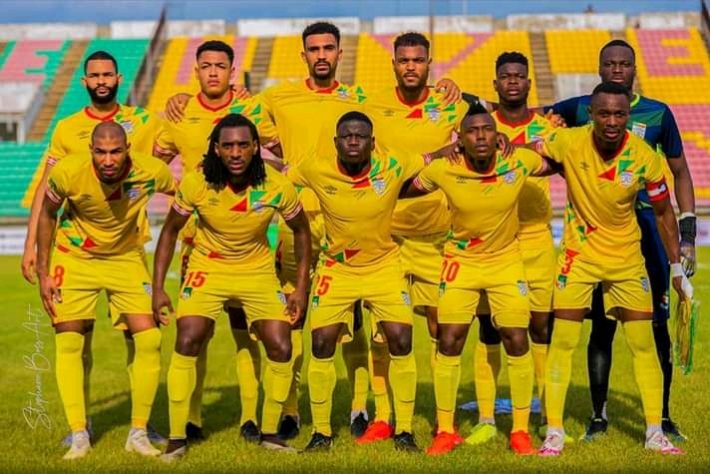 Onze joueurs en tenue sportive jaune posent ensemble sur un terrain de football dans un stade avec des gradins vides en arrière-plan