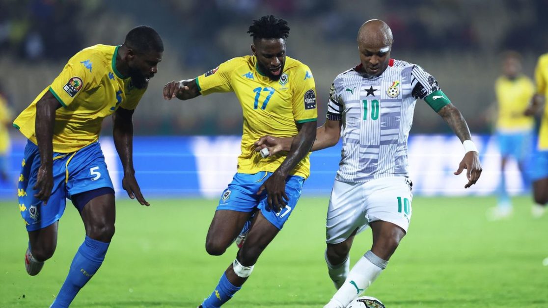 Trois joueurs de football en action sur un terrain, deux en maillots jaunes et un en maillot blanc contrôlant le ballon