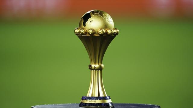Trophée doré posé sur un socle noir avec un fond flou de terrain vert et rouge