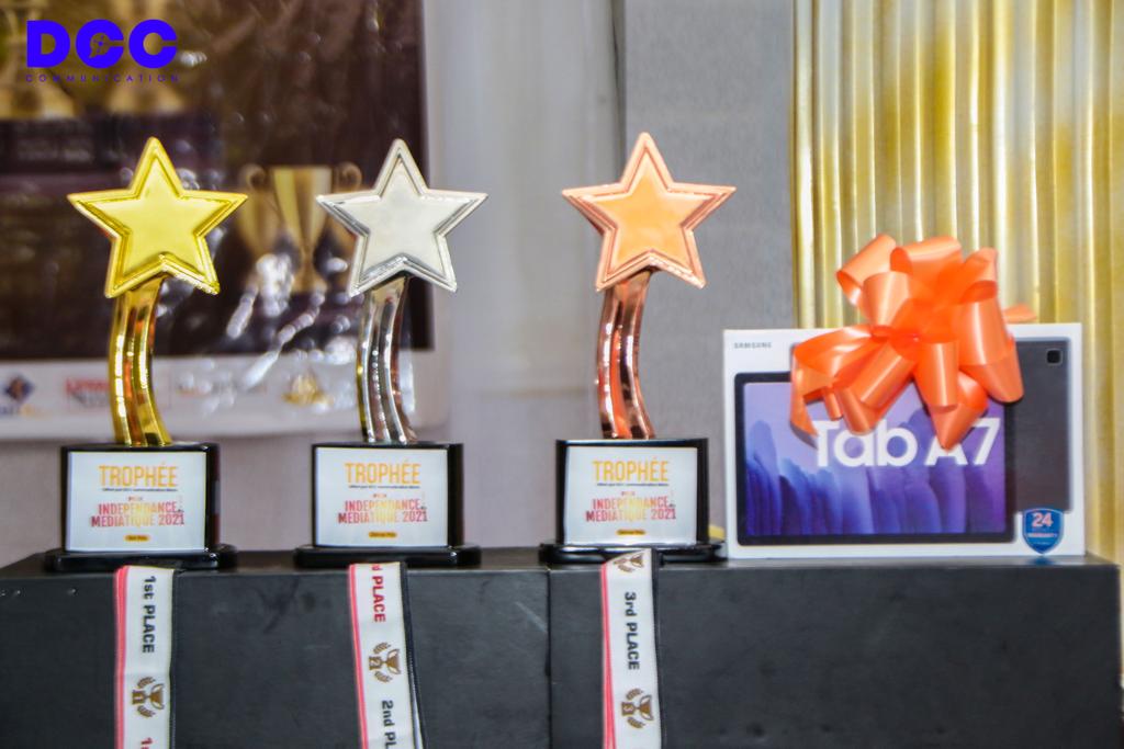 Trois trophées en forme d’étoile en or, argent et bronze alignés devant une boîte cadeau décorée d’un grand nœud rouge