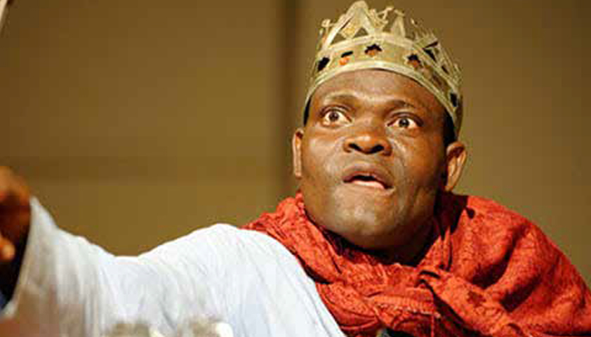 Homme au visage expressif portant une couronne et un vêtement rouge en pleine performance théâtrale