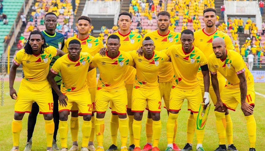 Onze joueurs de football en tenue jaune posent sur un terrain de stade avec des tribunes colorées en arrière-plan