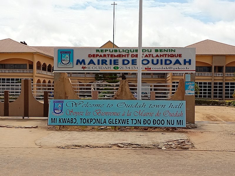 Façade d un bâtiment administratif avec panneaux annonçant la mairie de Ouidah en plusieurs langues