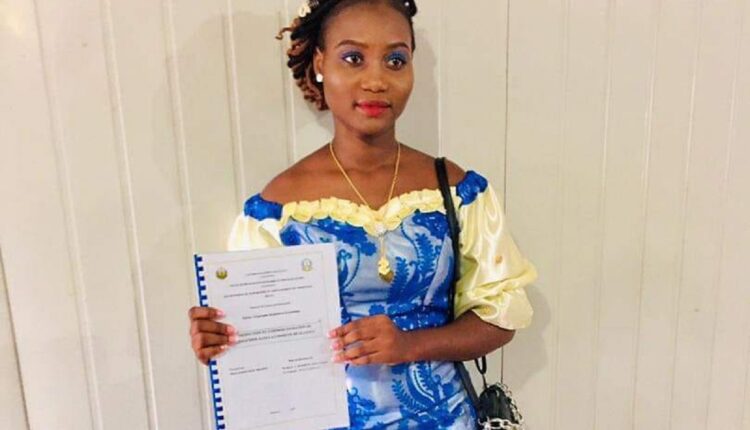 Jeune femme en robe traditionnelle bleue et jaune tenant un document relié devant un mur clair