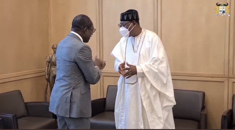 Deux hommes échangent avec respect dans un bureau aux murs clairs entourés de fauteuils en cuir noir