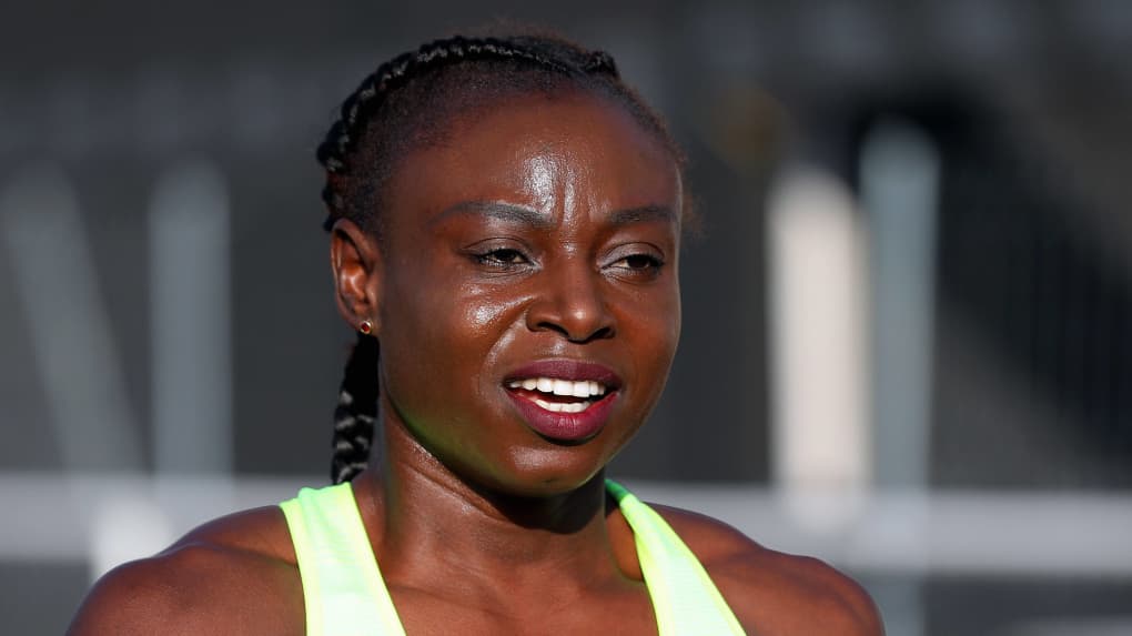 Athlète féminine en tenue de sport fluorescent sous la lumière du jour avec arrière-plan flou.