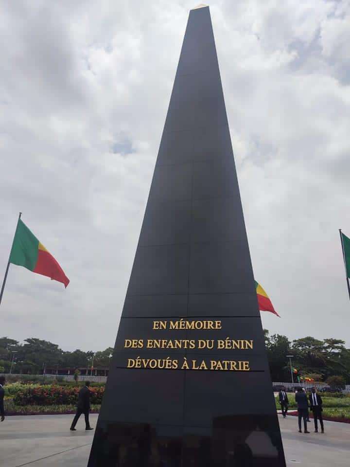 Obélisque noir avec inscription dorée en mémoire des enfants dévoués entouré de drapeaux colorés et de personnes au sol