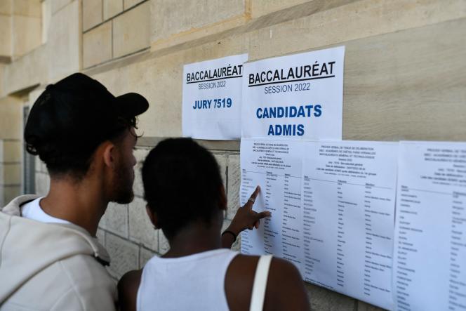 Deux jeunes consultent une liste de candidats admis au baccalauréat collée sur un mur en pierre