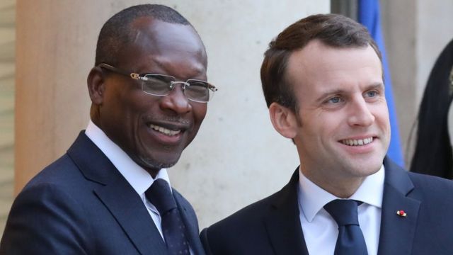 Deux hommes en costume souriant, debout côte à côte dans un cadre officiel avec un mur en arrière-plan