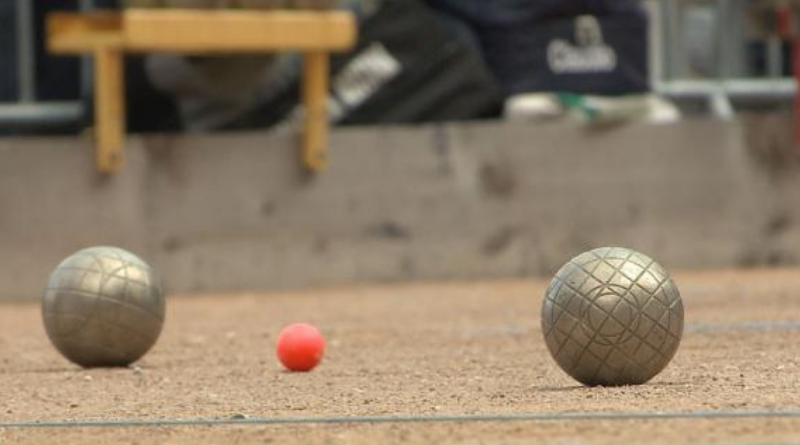 Deux boules de pétanque en métal entourant un cochonnet rouge sur un terrain de sable compacté