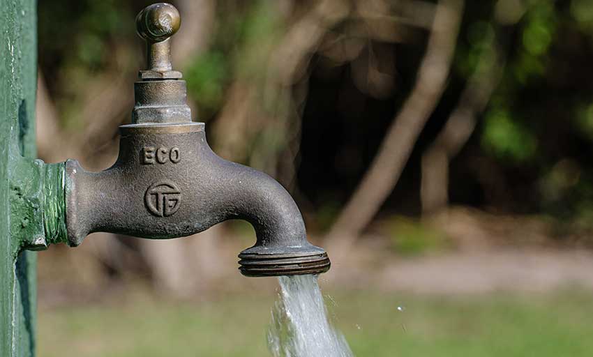 Robinet en métal vert avec de l'eau claire qui coule dans un environnement extérieur flou verdoyant