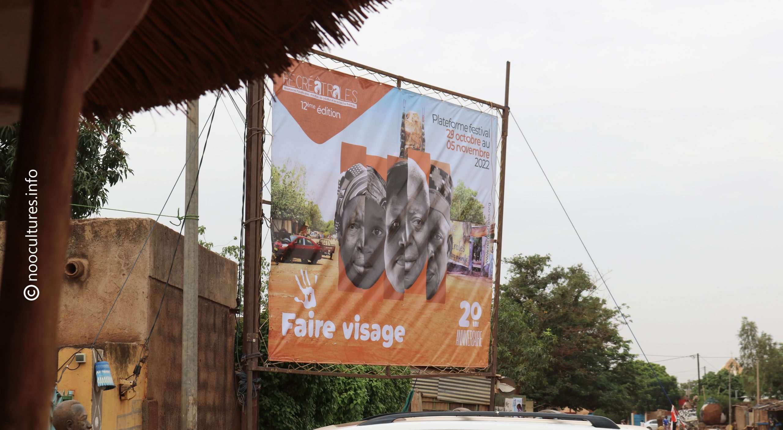 Affiche suspendue à une structure en bois montrant trois portraits en noir et blanc sur fond orange avec un texte en français