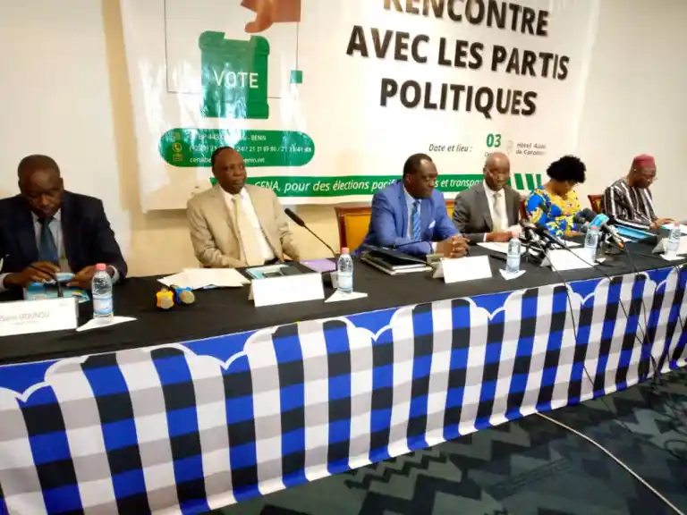 Cinq personnes assises derrière une table noire ornée d'une nappe à carreaux bleus et blancs avec micro et bouteilles d'eau devant elles