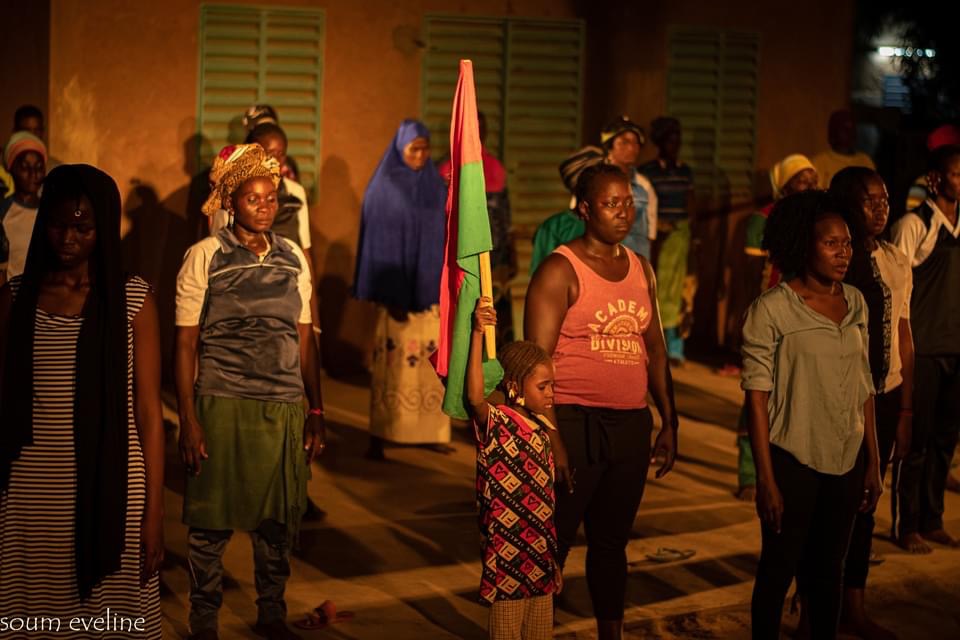Groupe de personnes debout dans une cour la nuit, un enfant tient un drapeau au centre du groupe