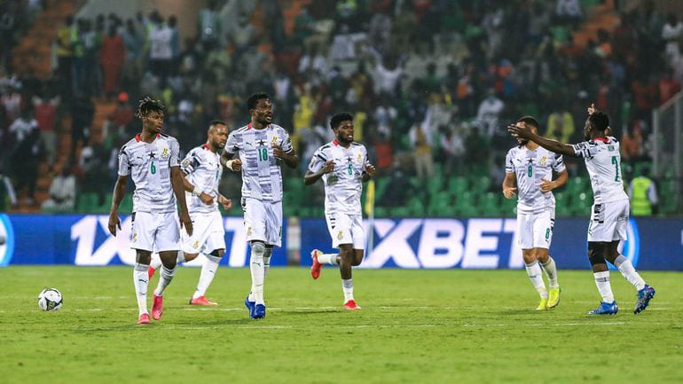 Cinq joueurs en tenue blanche sur le terrain de football pendant un match avec un public en arrière-plan