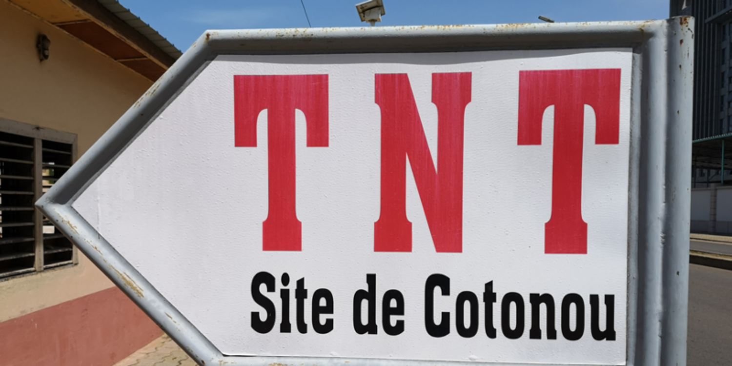 Panneau fléché indiquant TNT Site de Cotonou en grosses lettres rouges et noires