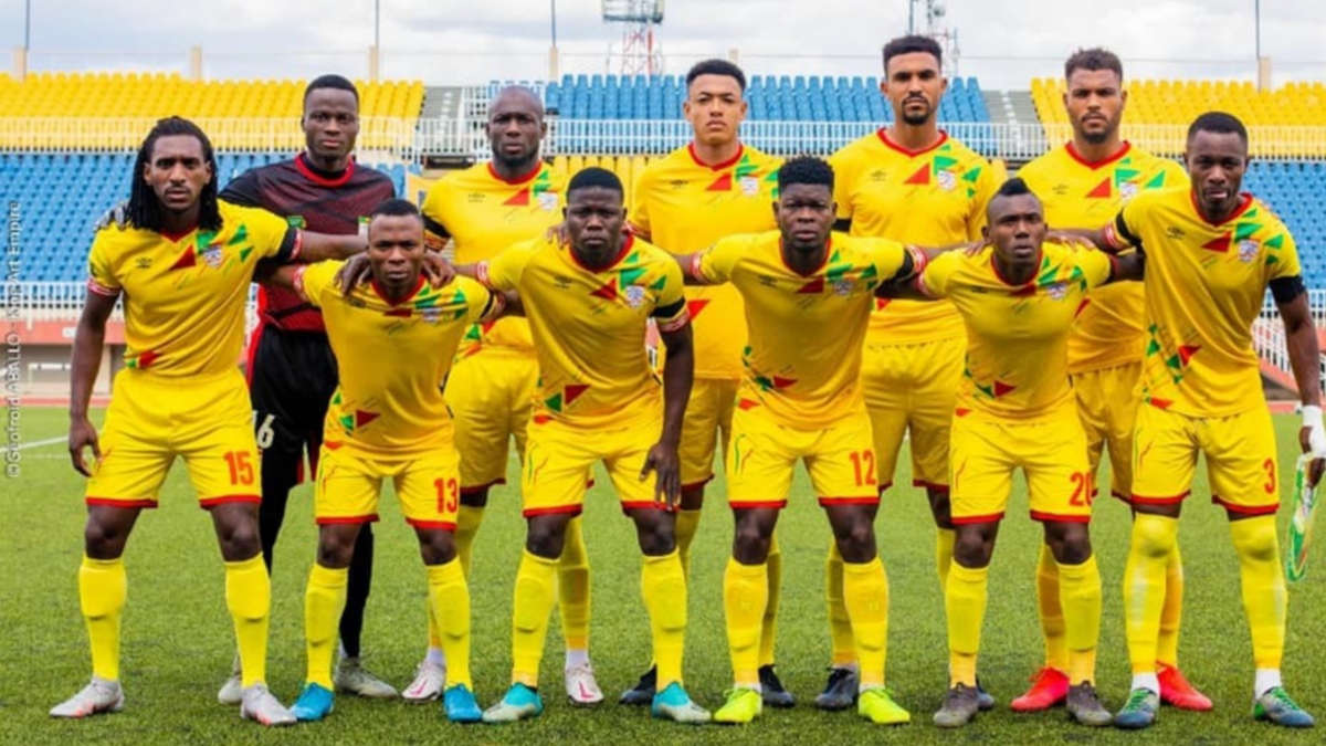 Onze joueurs de football en tenue jaune posent sur un terrain avec des gradins jaunes et bleus en arrière-plan
