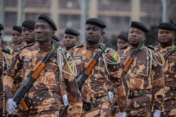 Des hommes en uniforme camouflage marron et noir avec bérets noirs défilent en rangs serrés dans la rue