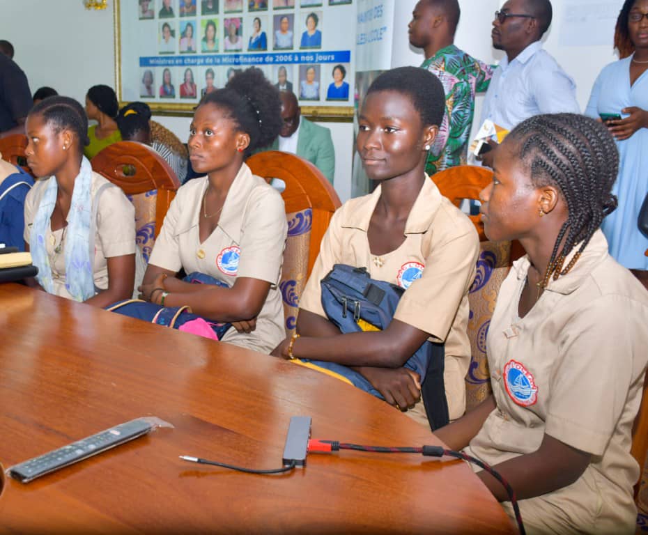 Des adolescentes assises à une table en réunion portant des uniformes scolaires beige avec badges circulaires colorés
