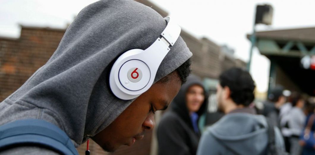 Jeune homme portant un sweat à capuche et des écouteurs blancs au milieu d'un groupe de personnes en extérieur