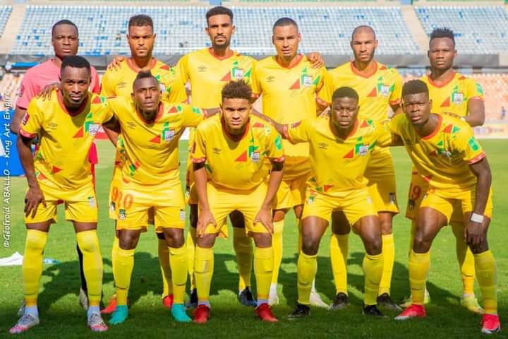 Onze joueurs de football en tenue jaune posant sur un terrain de stade avec gradins vides en arrière-plan