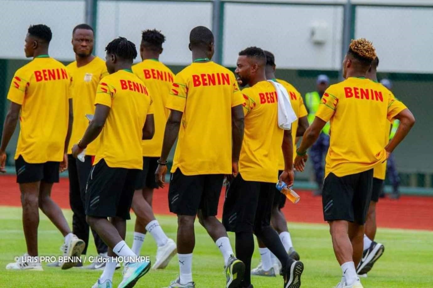 Des joueurs en maillots jaunes avec l'inscription BENIN marchent sur un terrain d'entraînement vert
