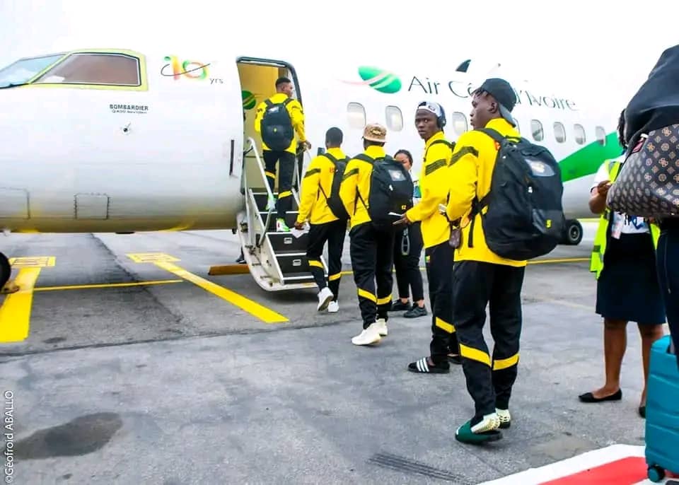 Des jeunes hommes en tenue jaune et noire montent dans un avion blanc marqué Air Caraïbes sur le tarmac