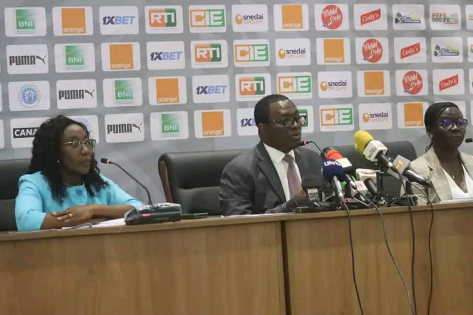 Trois personnes assises derrière un pupitre lors d’une conférence de presse avec plusieurs micros visibles