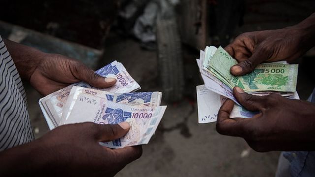 Deux paires de mains échangent et comptent des billets de banque en devises africaines dans un environnement urbain.