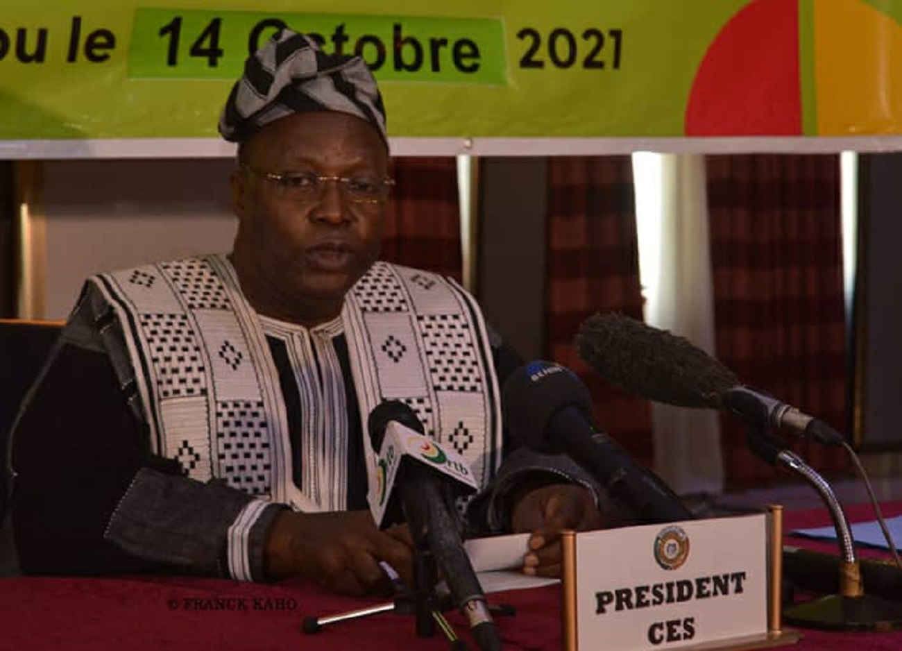 Un homme en tenue traditionnelle s’exprime derrière un pupitre avec un panneau PRESIDENT CES et plusieurs micros devant lui