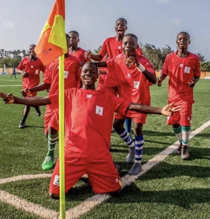 Des jeunes joueurs en maillot rouge célèbrent un but près du drapeau de coin sur un terrain de football en gazon synthétique