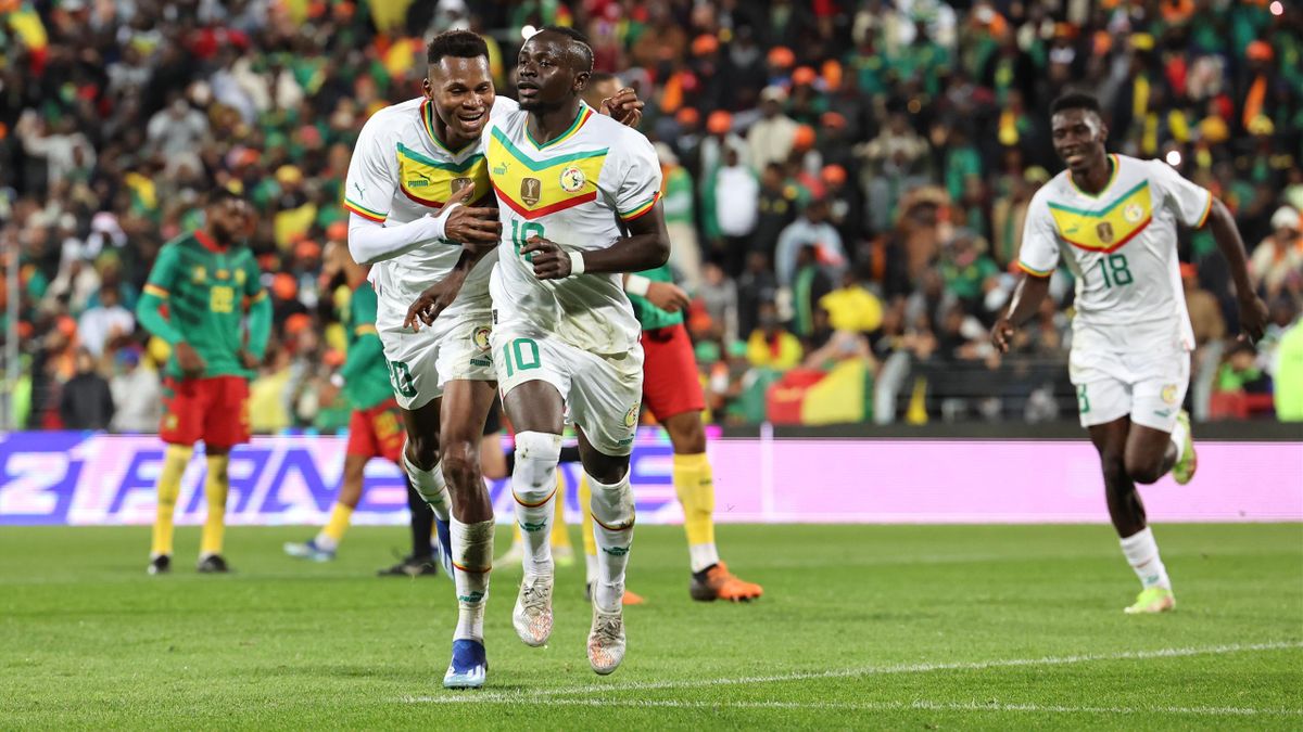 Trois joueurs en maillots blancs et verts célèbrent un but devant un public nombreux dans un stade de football
