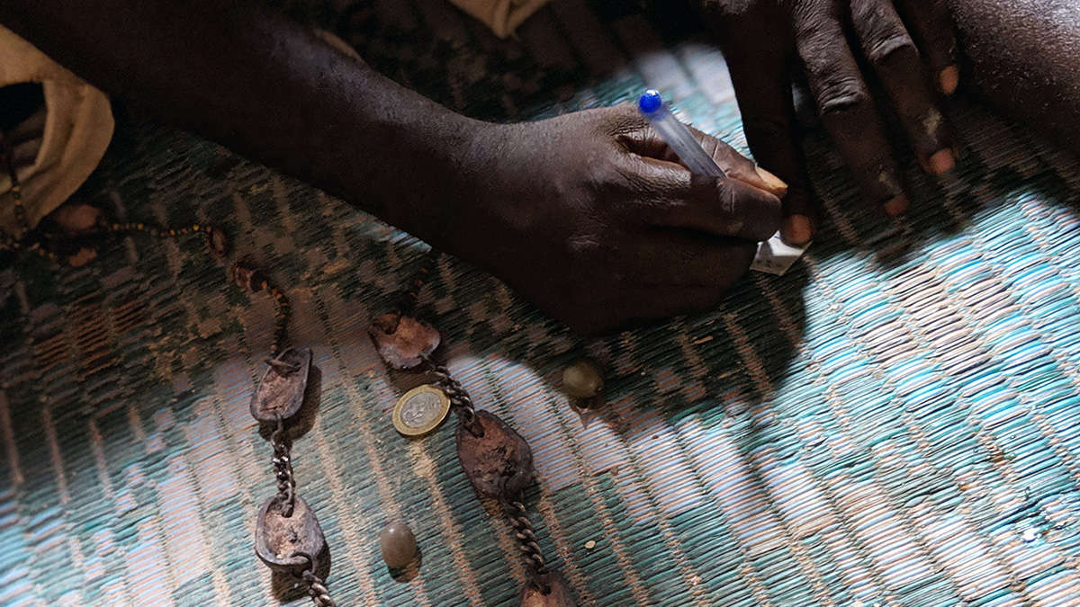 Main d une personne sombre tenant un stylo au-dessus d un tapis avec chaînes rouillées et une pièce de monnaie posées dessus