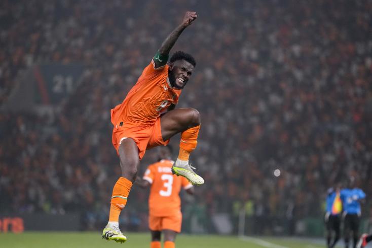 Un joueur en maillot orange célèbre un but en sautant avec le poing levé devant une foule dense au stade