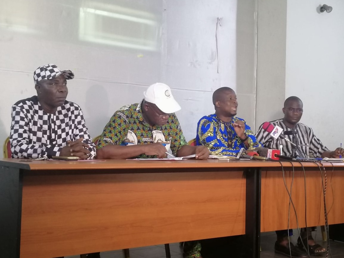 Quatre hommes assis derrière une table lors d'une conférence avec des microphones posés devant eux.