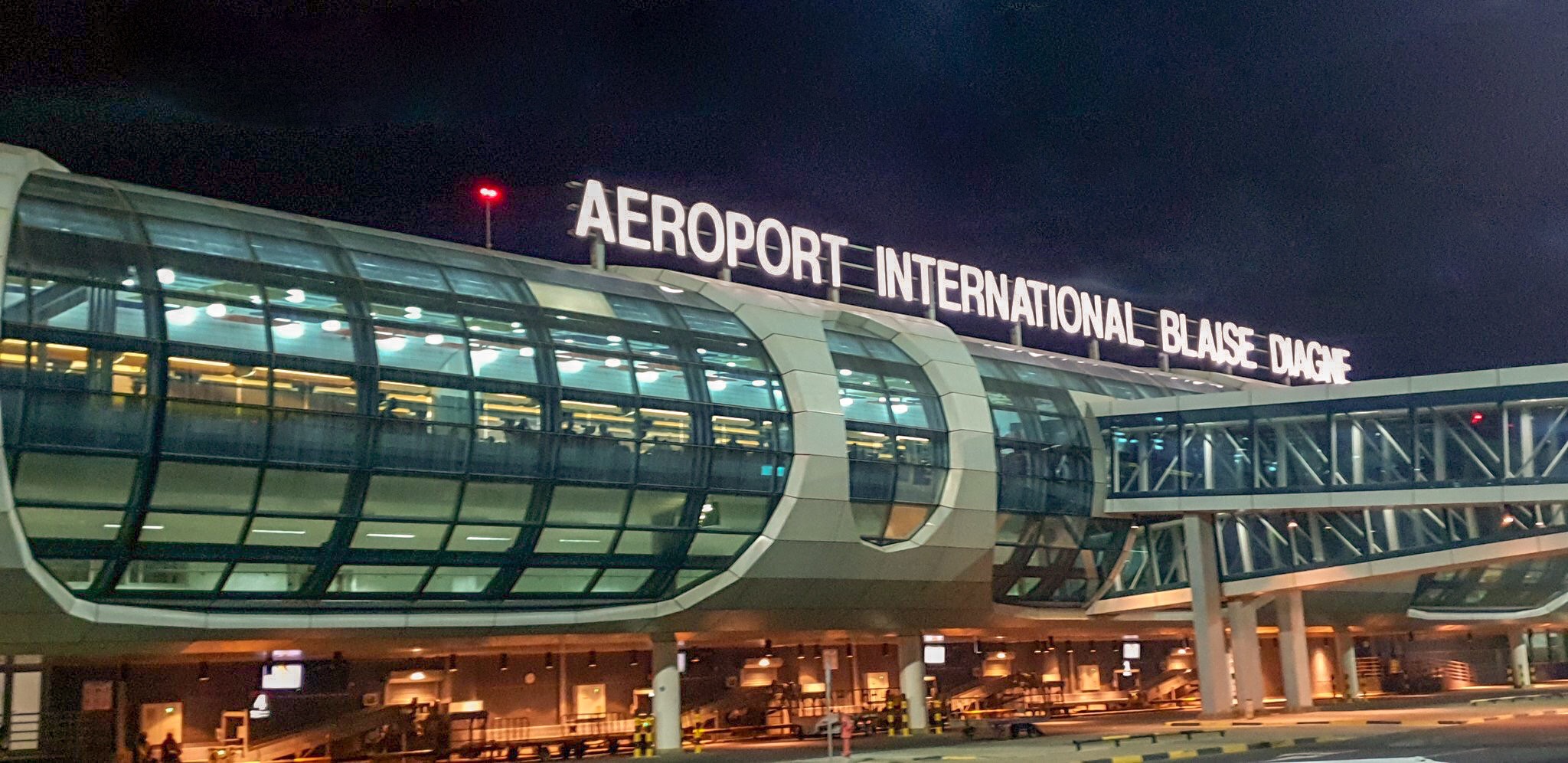 Façade extérieure éclairée d’un terminal aéroportuaire de nuit avec inscription lumineuse AEROPORT INTERNATIONAL BLAISE DIAGNE