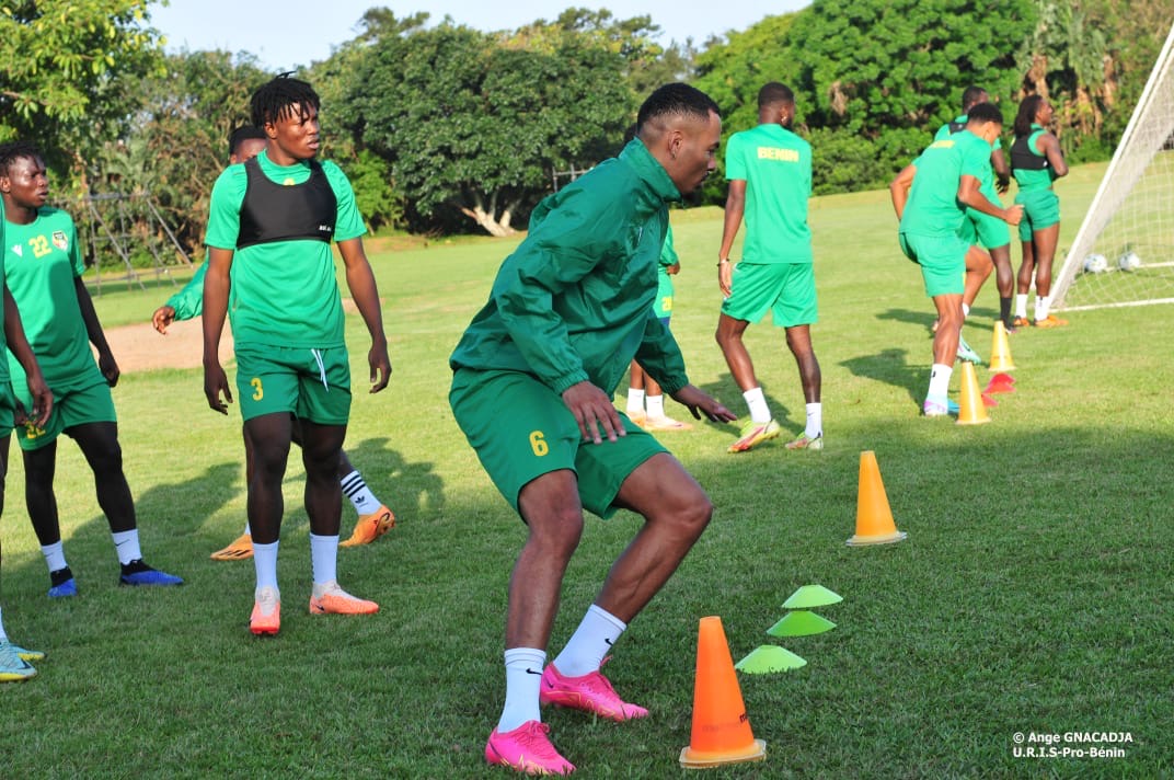 Des joueurs de football en tenue verte réalisent des exercices d'agilité sur un terrain herbeux avec des plots colorés