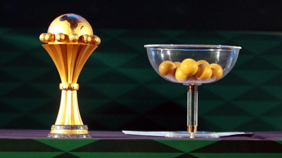 Trophée doré à gauche et récipient transparent contenant des boules jaunes sur une table à damiers verts