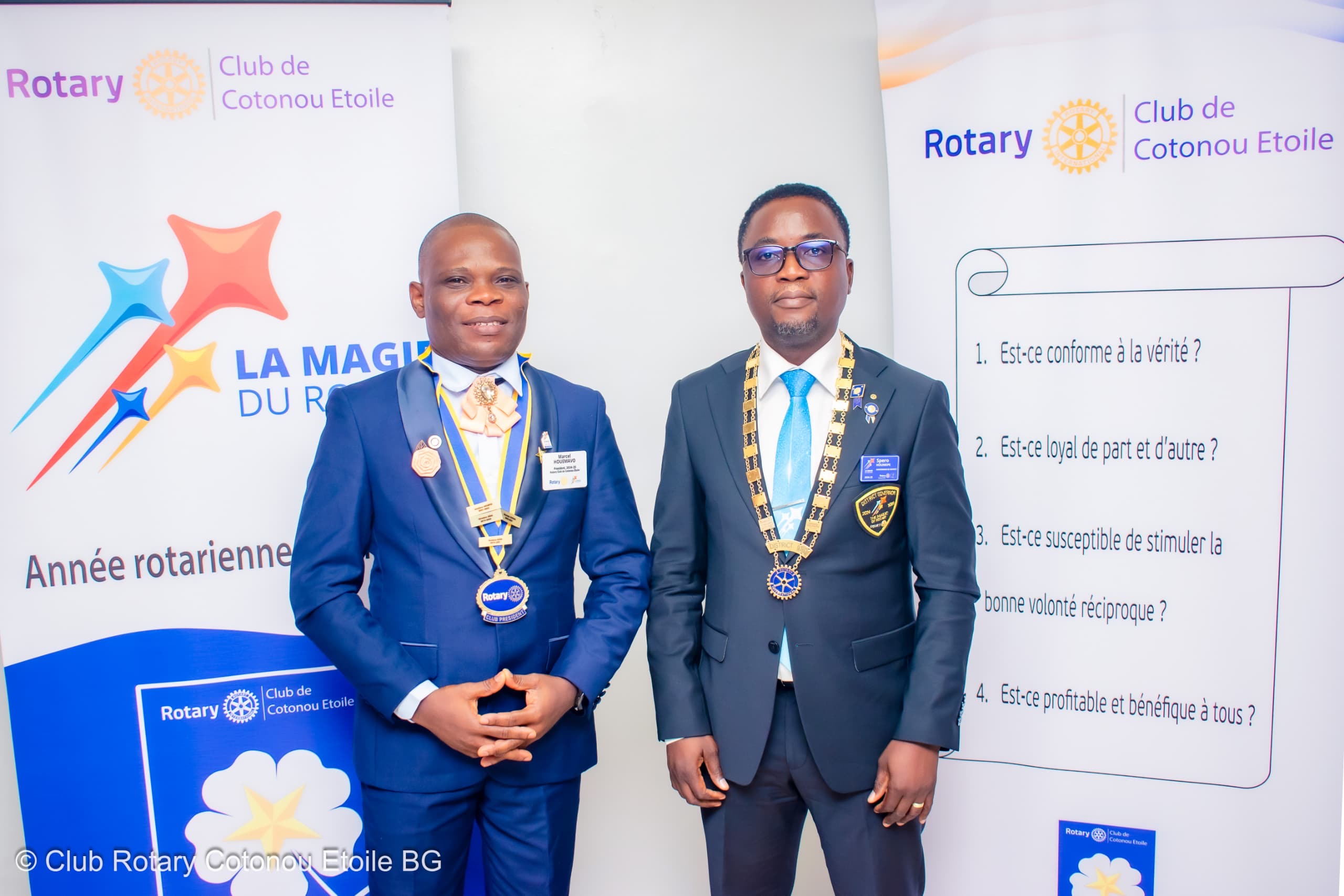 Deux hommes en costume posent devant des kakémonos du Rotary Club avec chaînes rituelles autour du cou