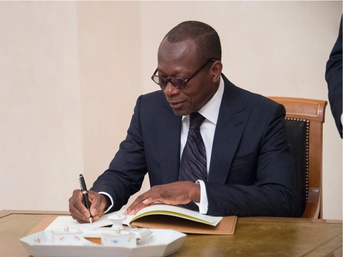 Homme en costume sombre signe un document posé sur une table avec une plate en porcelaine devant lui